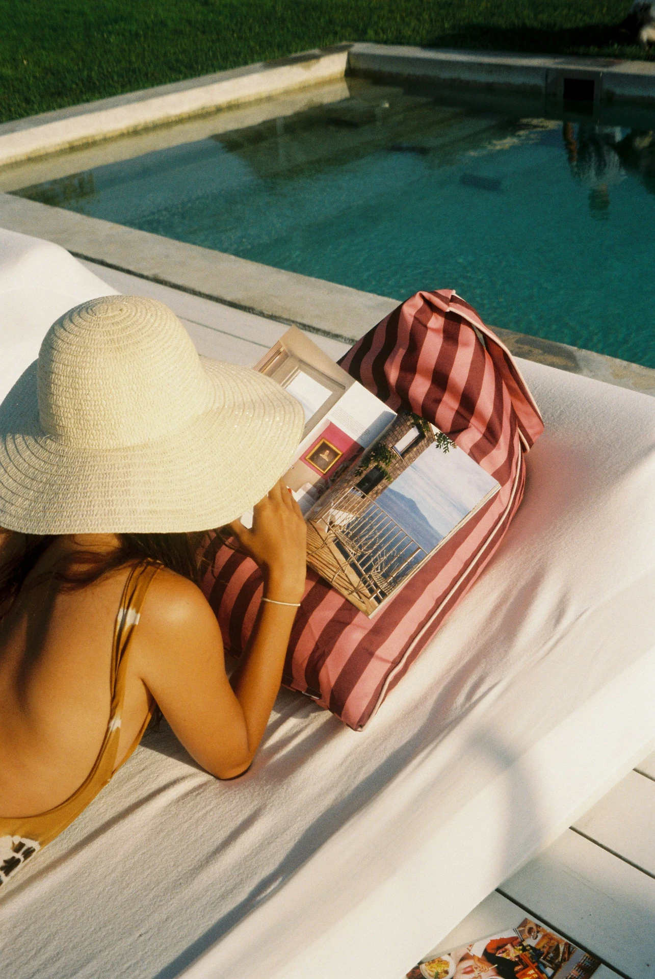 Lielow East Hampton — model in a straw hat lounging on the striped bag by a pool