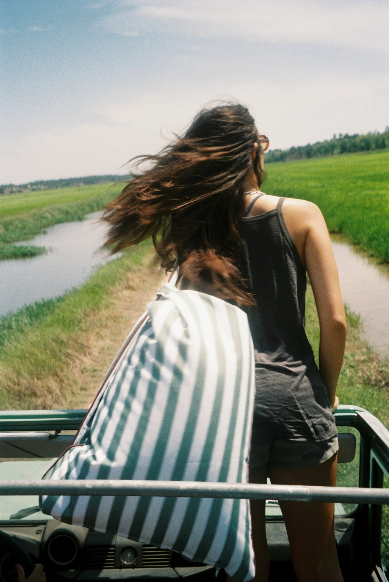 LIELOW Tribeca — model carrying the sage striped bag standing in an open-top Land Rover