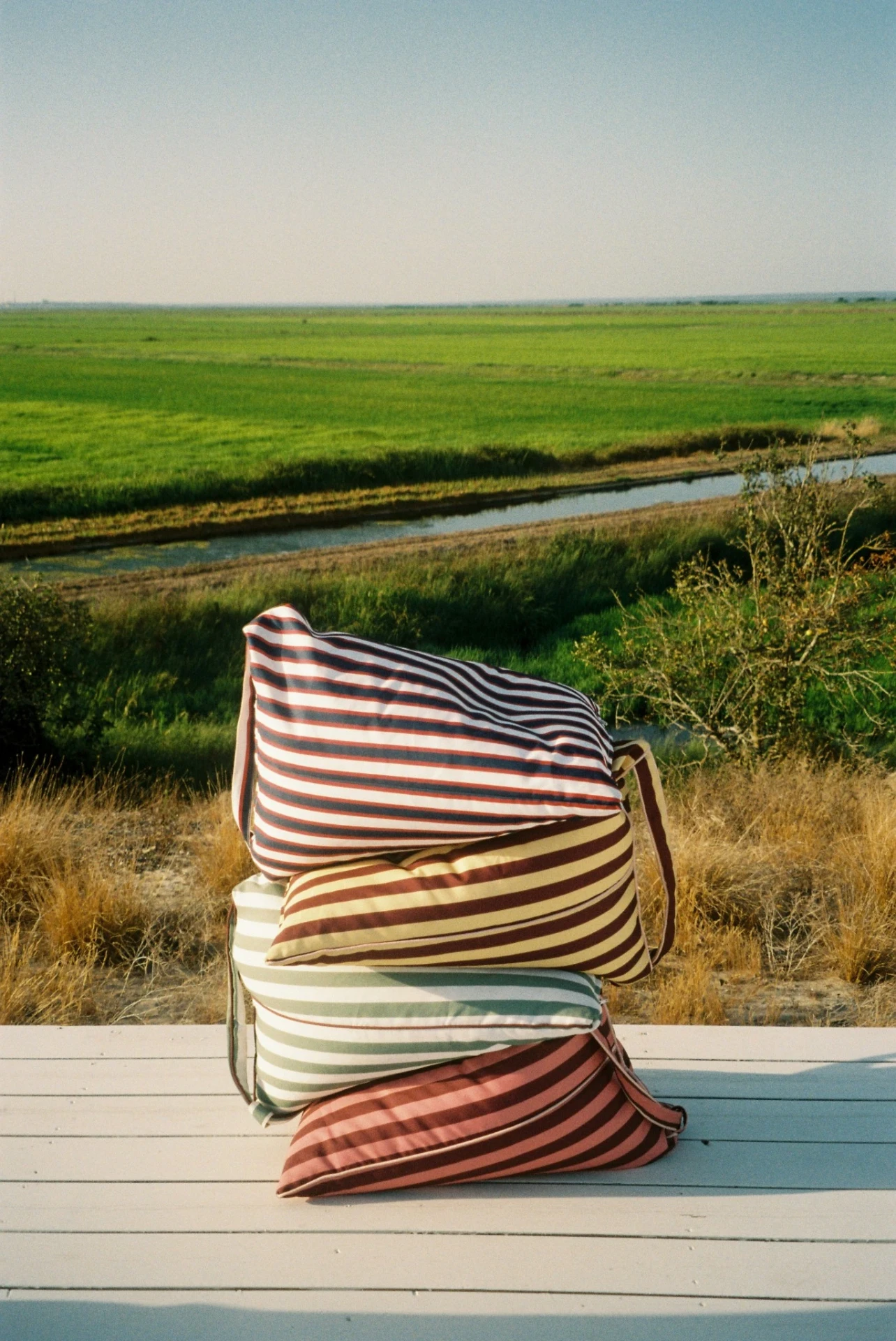 Stack of LIELOW striped backrests on a deck overlooking green fields