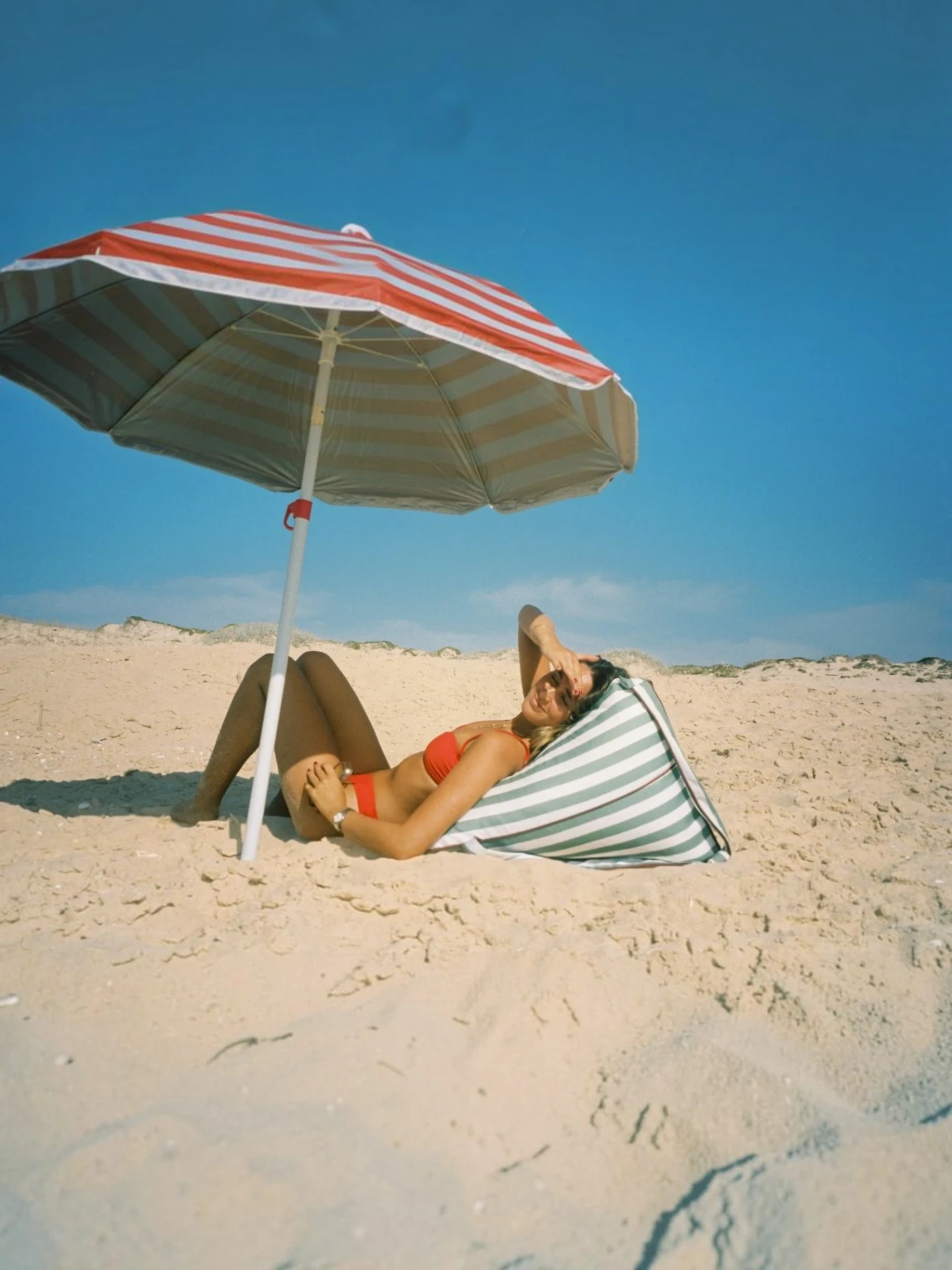 LIELOW Tribeca — model lounging on the sage striped bag-chair on the sand under a beach umbrella