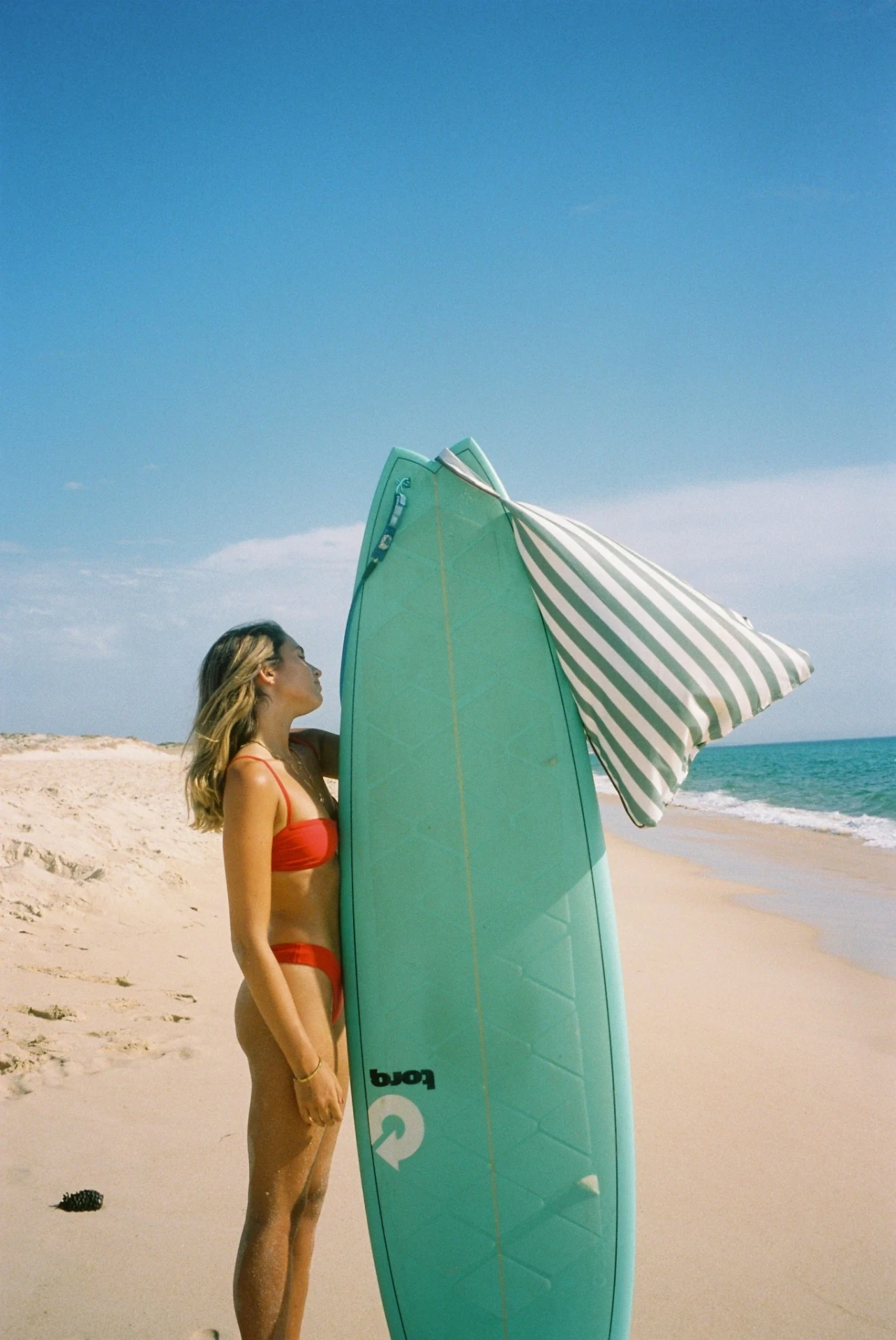 LIELOW Tribeca — sage striped bag draped over a surfboard on the beach