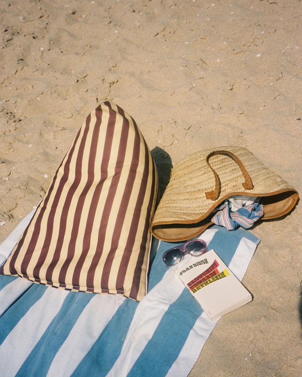 Pier 55 backrest on a striped towel with a straw basket, sunglasses and a book