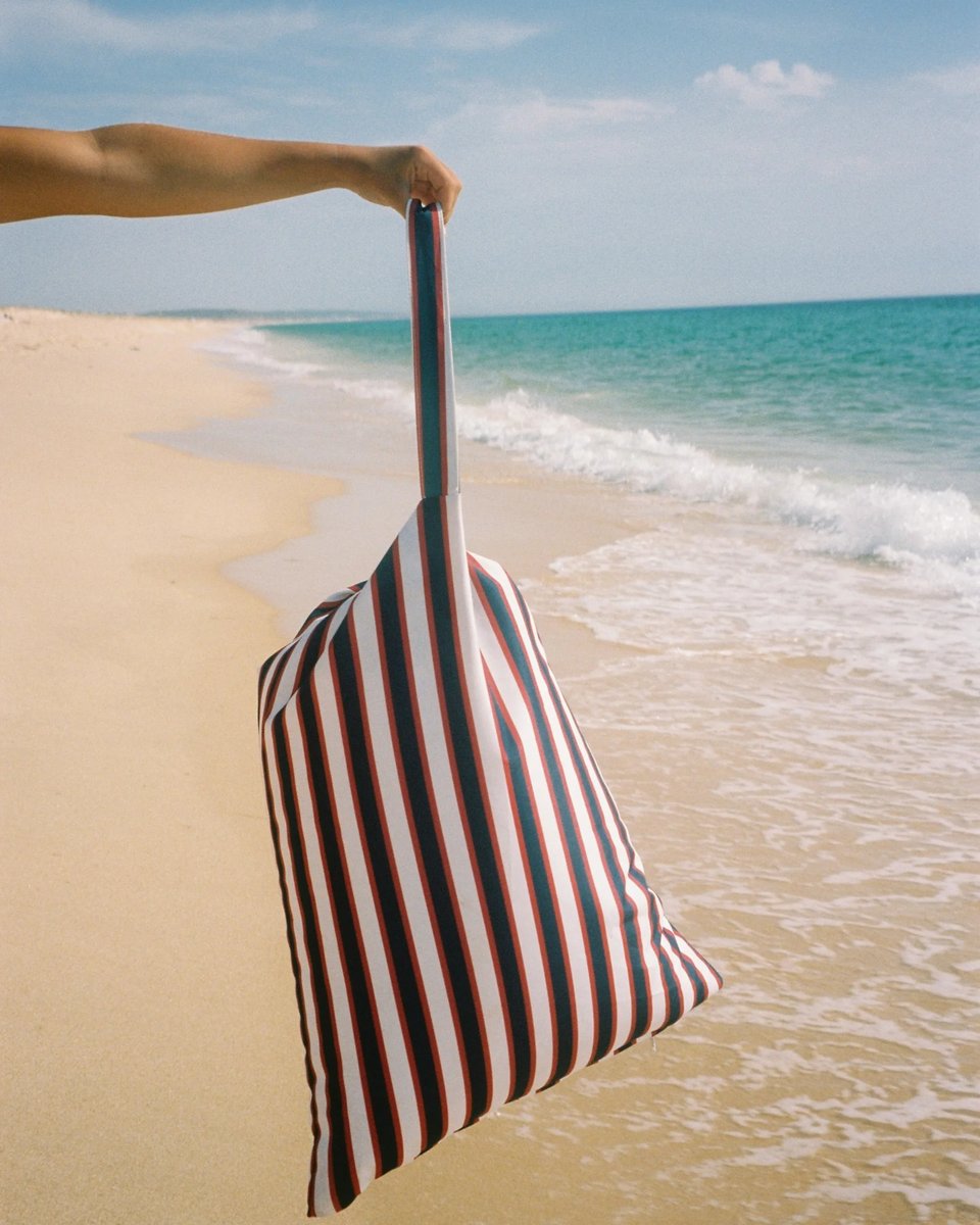 Montauk backrest held by its strap in one hand at the shoreline