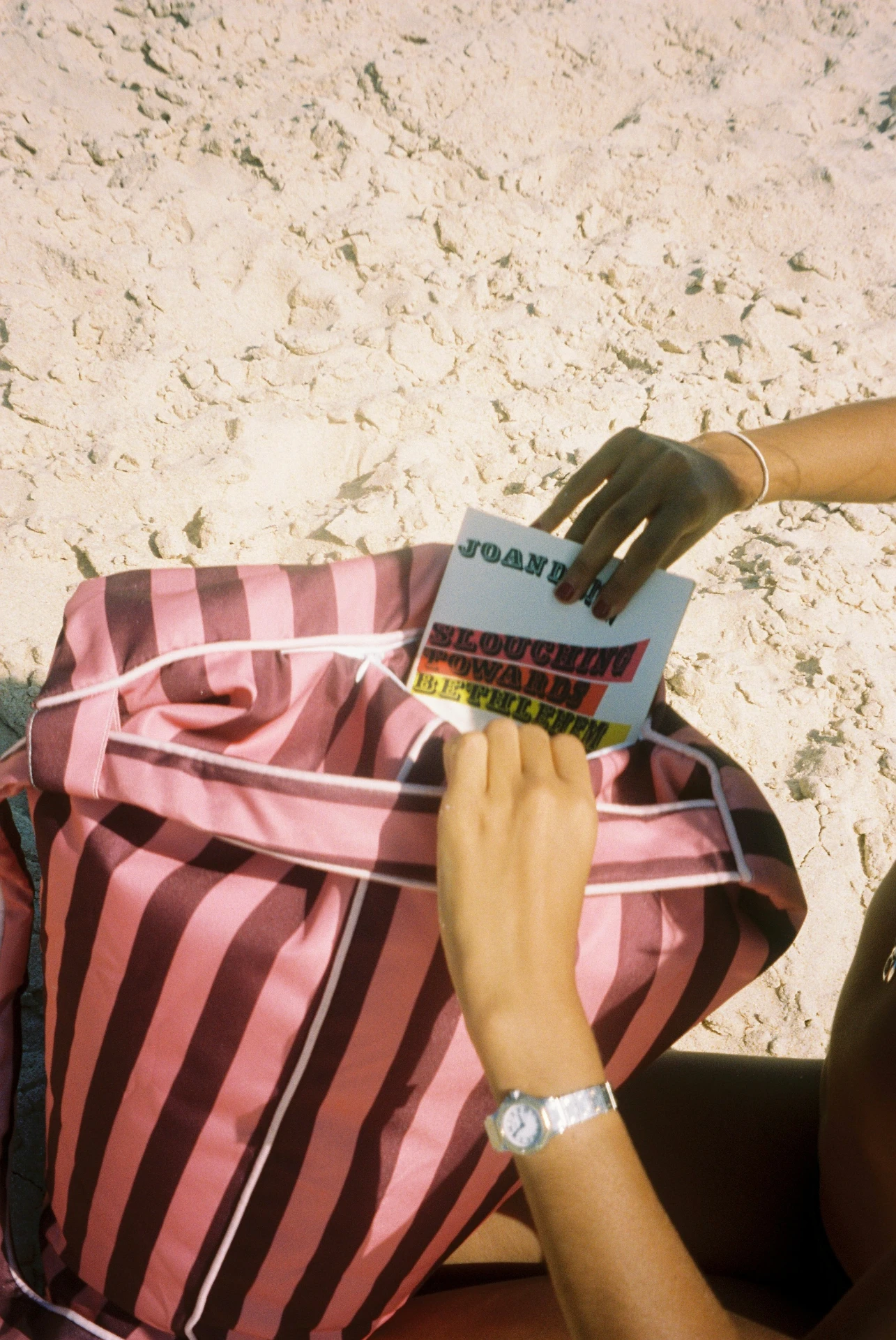 Lielow East Hampton — hands pulling a book from the striped bag on the beach